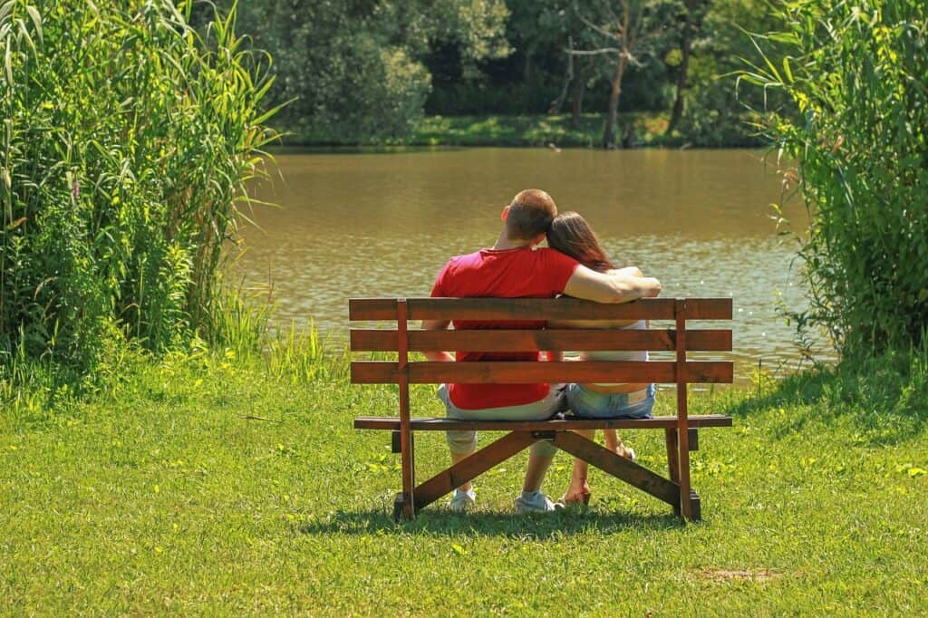 Couple on bench by a lake arms around